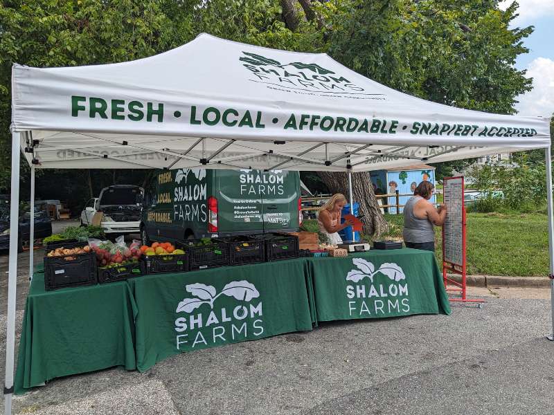 two people set up the shalom farms market stand