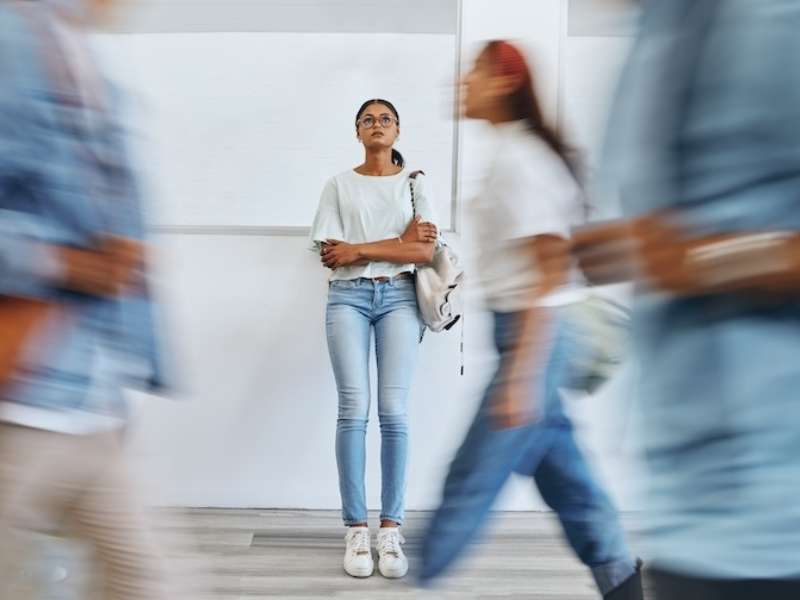 a young woman stands alone while passersby move around her in a blur