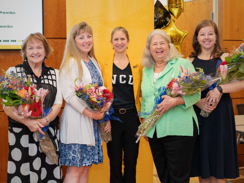 dean of v.c.u. school of nursing standing with four smiling award recipients holding bouquets of flowers at an awards ceremony