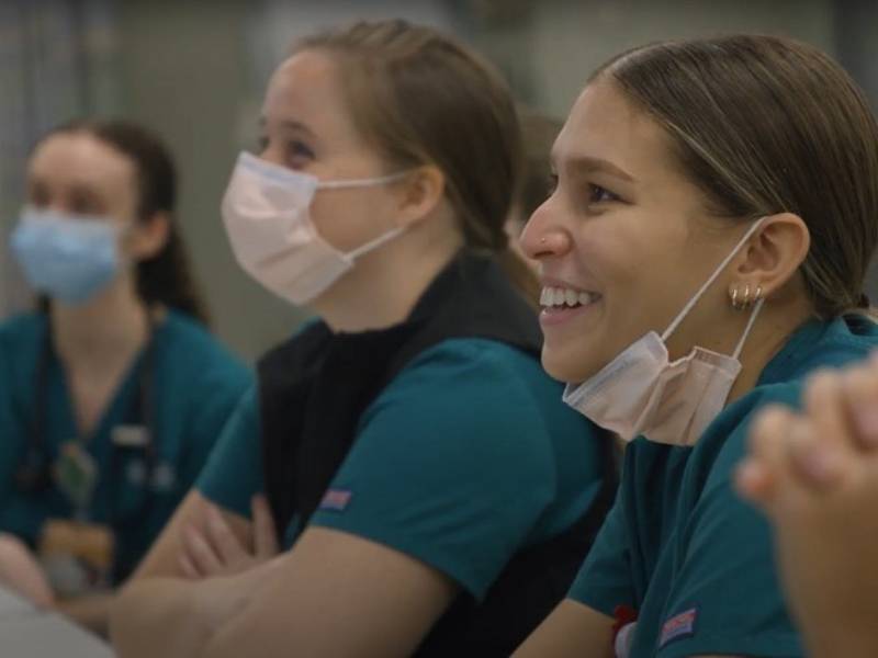 v.c.u. nursing students sitting at a table in class smile at their instructor